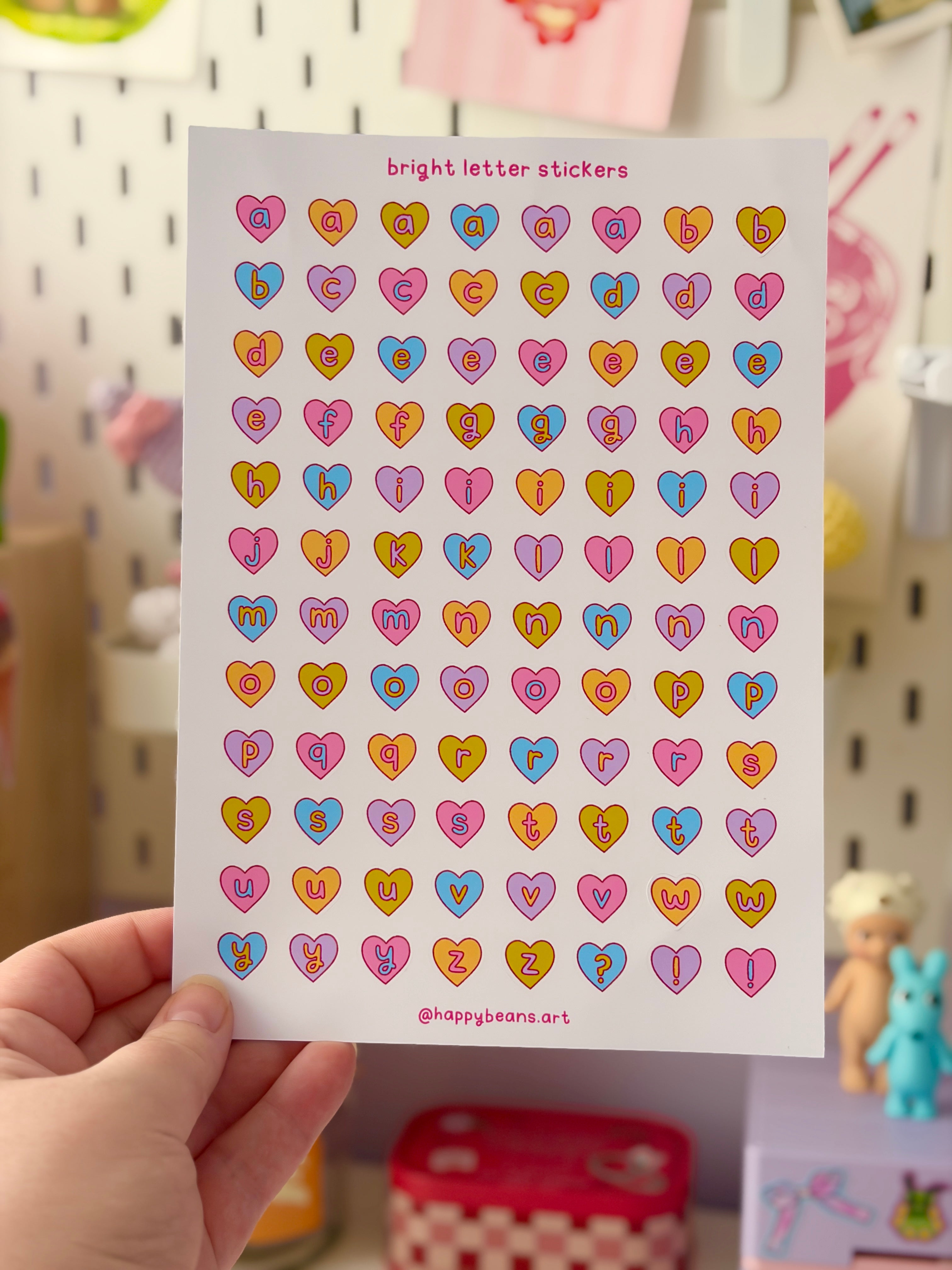 Sheet of colorful heart-shaped letter stickers held by a hand with a blurred background.