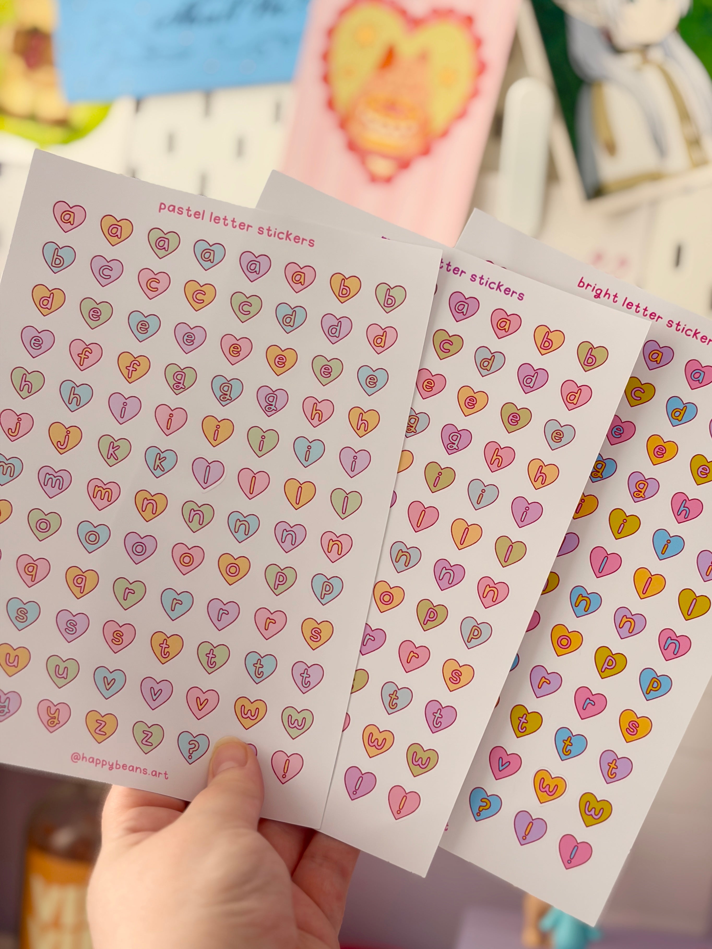 Three sheets of colorful heart-patterned stickers held by a hand with a blurred background.
